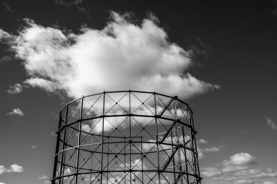 Monochrome sky and cloud frame an industrial architecture structure where metal framework forms a bold silhouette with strong contrast