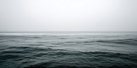 Fototapeta premium Minimalist coastal scene under pale overcast daylight with a quiet grey sea meeting a soft grey sky at a blurred horizon line