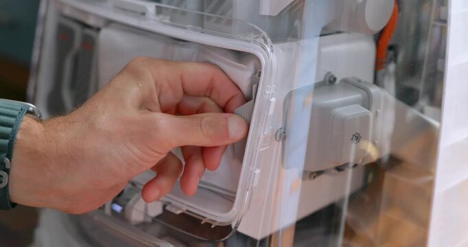 Close-up of hands opening a robot vacuum dock and removing the dust filter bag from the compartment