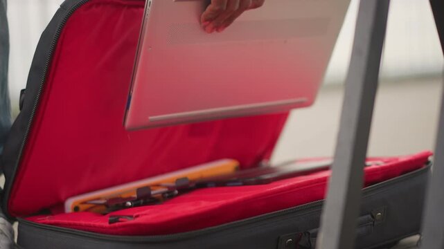 street musician packing controller into red case, jeans and sneakers visible, hands adjust mixer and cables, zipper closes over portable gear on sidewalk, candid urban preparation before performance