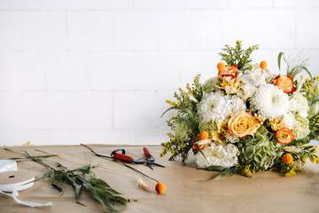 Obraz premium Large flower arrangement rests on florist workbench near garden shears and ribbons. Boutique florist, local business owner, craft economy, handmade floral arrangements.