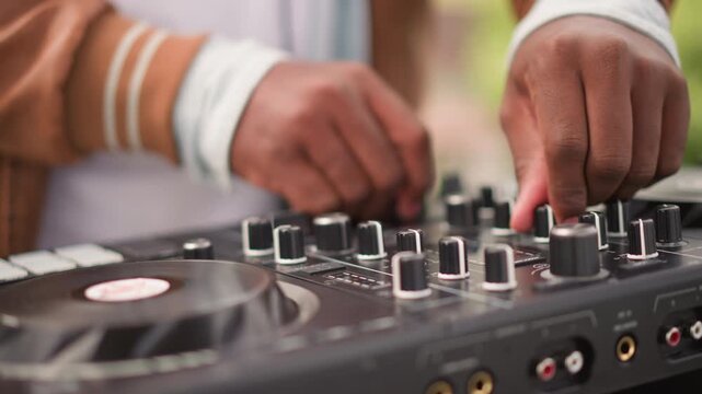 Closeup black DJ hand adjusting knob on controller, lively backyard party vibe, crisp daylight, energetic tempo changes, vinyl jog wheel and tactile fader moves, casual entertainer connecting