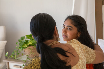 Indian mother and daughter wearing orange sari sharing embrace at home with wooden table © wavebreak3