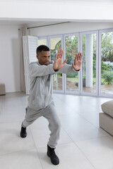 Naklejka premium African american man practicing martial stance in living room by glass doors