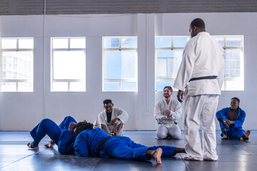 Diverse martial class with instructor practicing sparring in gis on mats in studio, copy space