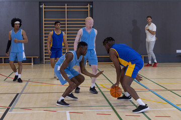 Naklejka premium Diverse male basketball players practicing under coach on court with ball, copy space
