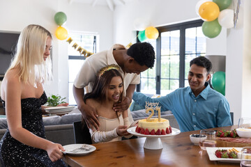 Diverse friends gathering at dining table at home celebrating birthday, happy birthday 21 cake