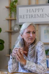 Fototapeta premium Senior woman sitting at table in decorated room under happy retirement sign with balloon