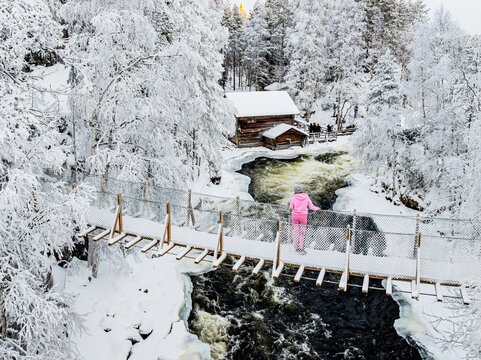 Woman looking at cold rapids from a snowy bridge