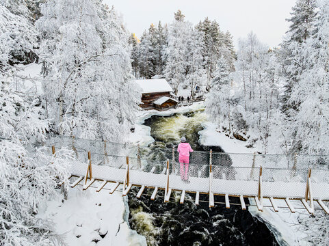 Woman on icy bridge watching watermill and rapids