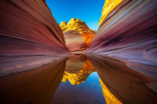 Sunrise at The Wave with hiker reflected in puddle