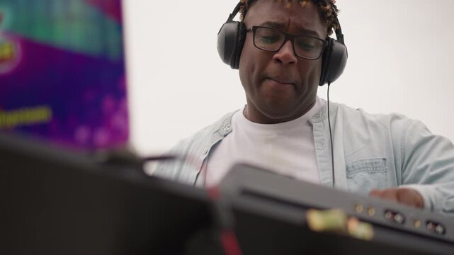 Black DJ performing energetic outdoor set with headphones and controller, dynamic gestures over mixer, engaged crowd energy, festival signage in background, headliner vibe and lively soundmix