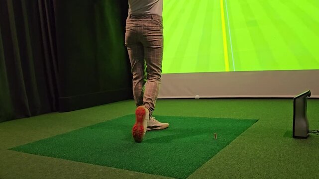 Golf practice session indoors on a simulator with a player preparing to swing