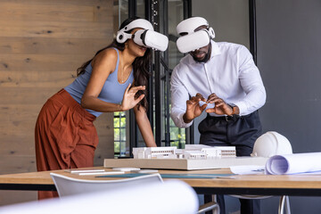 Diverse team wearing business attire and vr headsets viewing model, blueprints, helmet in office