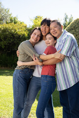 Diverse family hugging each other wearing casual clothes in backyard garden under sunlight