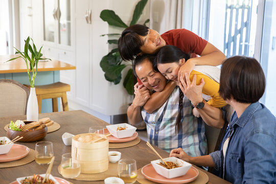 Diverse family hugging around dining table at home with noodles, chopsticks and wine glasses