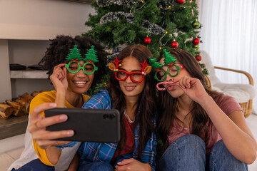 Naklejka premium Diverse female friends posing for selfie on living room floor with smartphone near christmas tree