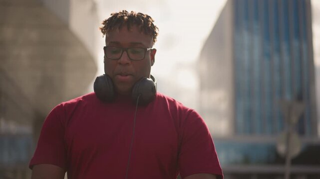 black man with headset in plaza, urban portrait under soft backlight pausing between sets, scouting corners, testing mixes, posing against modern architecture, contemplative gaze and relaxed