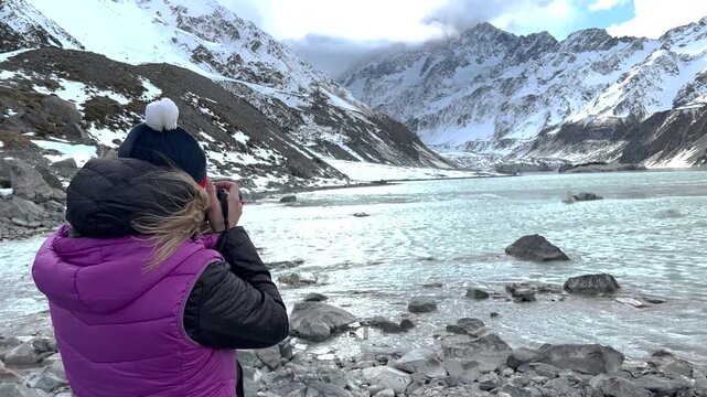 Woman taking photos of Mount Cook mountain and Hooker Lake, Winter New Zealand snow.