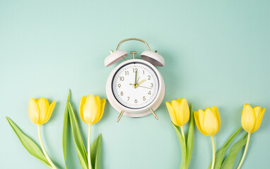 Switch to daylight saving time in spring, summer time changeover, alarm clock with yellow tulip flowers