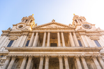 Naklejka premium St. Pauls Cathedral stands tall in London. Visitors gather around the front portal. The sun shines on the historic building, highlighting its impressive architecture.