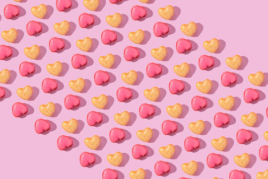 Heart shaped pink and yellow macarons in a repeating pattern on pink