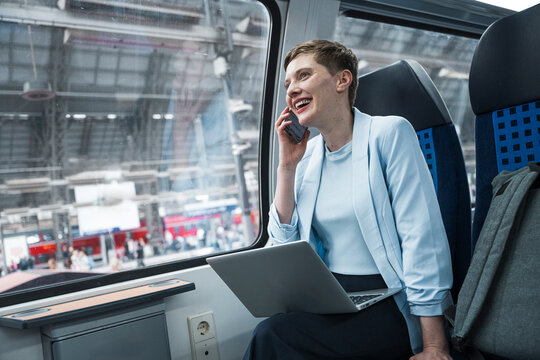 Businesswoman using mobile and laptop in train compartment at station