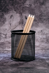 Three newly sharpened wooden pencils stand proudly in a minimalist black mesh holder