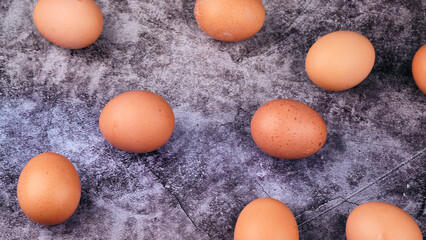 A collection of natural brown eggs softly spreads across a dark, stone-like textured surface. Each egg displays unique specks, ready for a delightful recipe