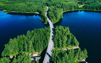 Obraz premium Aerial View of Serene Winding Road Overlooking Dense Forest and Tranquil Blue Lakes in Finland
