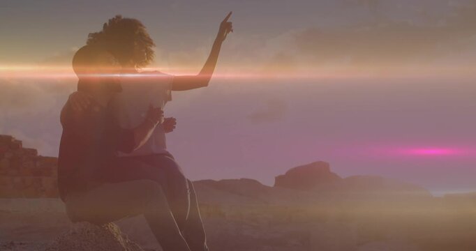 Light trails against african american couple pointing towards a direction sitting on the rocks
