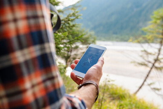 Young man navigating outdoors with compass app on cell phone