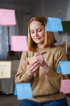 Woman writing positive affirmations on sticky notes for well being