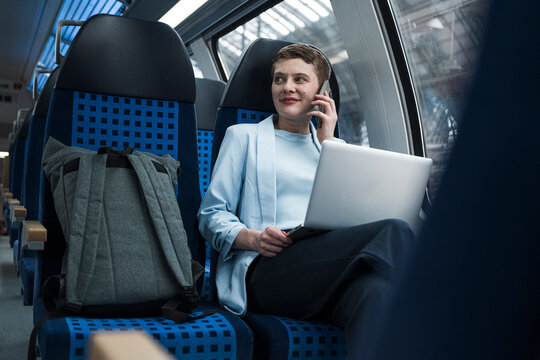 Businesswoman working with laptop and talking on mobile in train compartment
