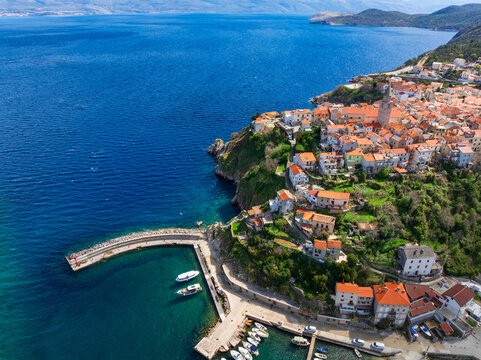 Drone captures stunning top view of Vrbnik towns on Krk Island in Croatia. Blue Adriatic Sea meets rocky coastline and traditional Mediterranean architecture from above.