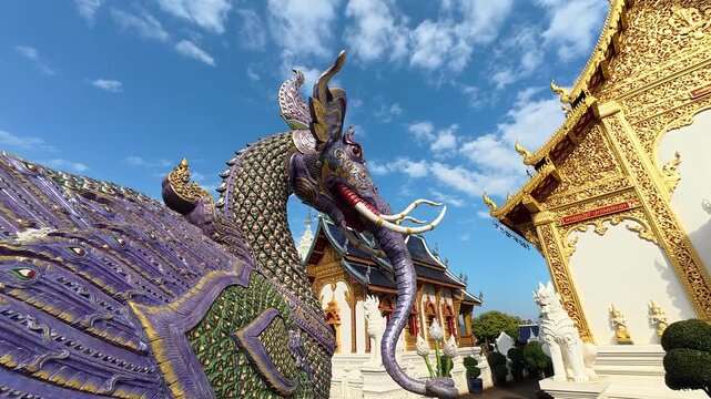 View of Wat Ban Den temple in Mae Taeng, Chiang Mai, Thailand. The video shows colorful Lanna style buildings, blue roofs, golden details and sacred pagodas rising above peaceful rural landscape.