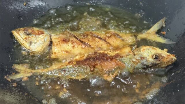 Close-up video of fresh fish being fried in a pan with hot oil. Crispy texture forming on the surface with oil splashes and steam. Traditional home cooking concept, Asian cuisine, food preparation pro