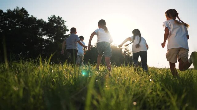 Children run across grass field into warm sun as child and kid play and laugh with friend in outdoor summer setting with bright sun glow over green grass tall grass sway and long shadow across field