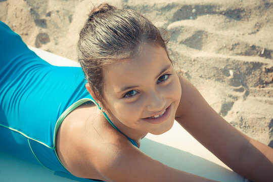 Close-up Portrait of smiling girl in a s swimming costume lying on a surfboard on a sandy beach