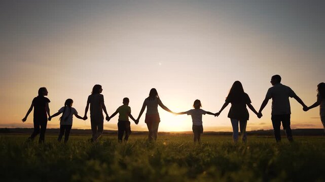 People holding hands together in sunset field silhouette showing family child unity outdoors with people and child walking hand in hand across grass under golden sky together and family bond