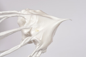 Obraz premium A thick glossy white whipped meringue mixture with a sharp stiff peak clings to the wires of a metal whisk against a neutral light background