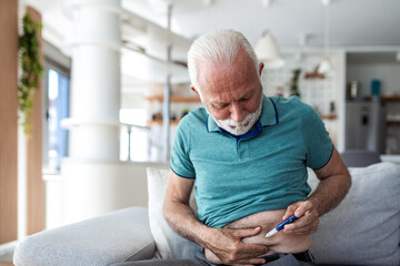 Insulin injection. Senior man with diabetes giving himself an insulin shot in the stomach with a pen. Elderly male patient injecting medication at home, healthcare and medicine concept. © Graphicroyalty