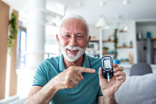 Successful glucose check. Happy senior man pointing at blood sugar monitor showing normal results. Smiling elderly male with diabetes holding glucometer, healthcare and medicine concept at home.