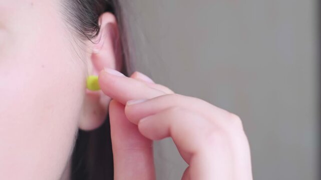 Close-up of a woman's hand squeezing earplugs before inserting them into the ear canal, preparing for sleep in a noisy city.