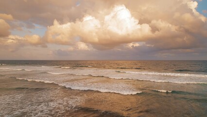 Golden sunset clouds reflect on ocean waves creating a tranquil seascape.