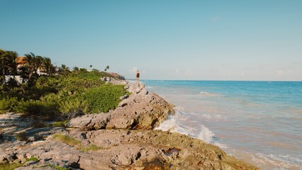 Solo traveler on jagged rocks admiring the expansive turquoise ocean in Mexico.