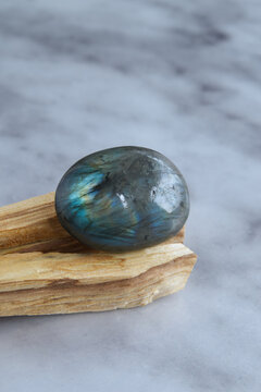 Polished labradorite stone with iridescent blue and green reflections, placed on a natural wooden base with a neutral background.
