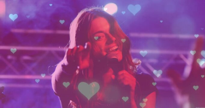 Singer moving at concert after dancer stepping back gripping mic engaging fans with heart overlays