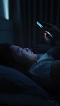 Asian woman lying in bed scrolling on her smartphone before bedtime, enjoying short-form video content on a digital platform