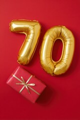 Naklejka premium Golden balloon number 70 with red gift box on red background